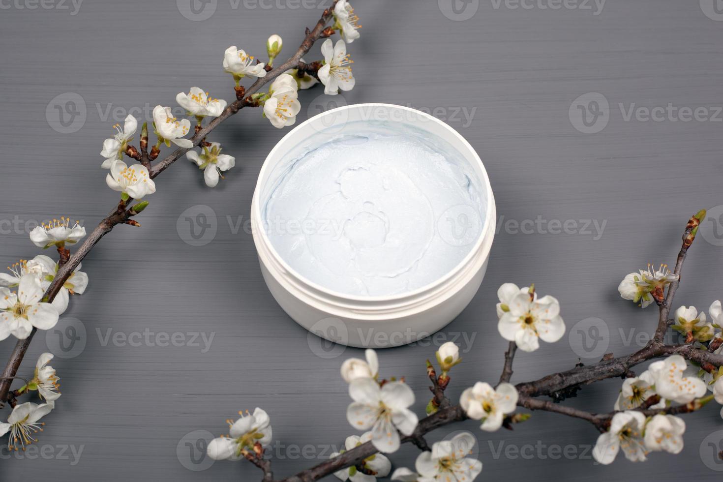 witte ronde bodyscrub met takken van witte bloemen op een grijze achtergrond foto