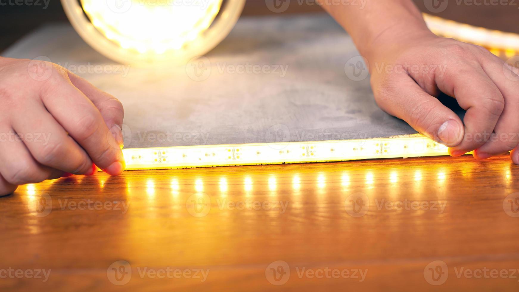 handen installeren een lichtgevende ledstrip close-up op een houten oppervlak foto