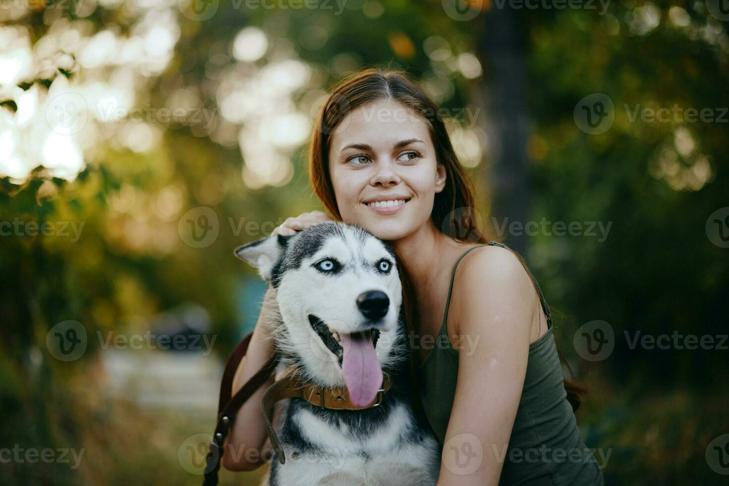 een vrouw met een schor ras hond glimlacht en liefdevol beroertes haar geliefde hond terwijl wandelen in natuur in de park in herfst tegen de backdrop van zonsondergang foto