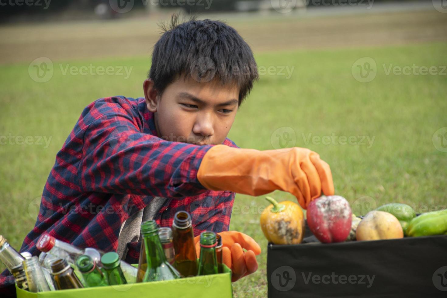 jong Aziatisch jongen sorteren divers vuilnis en zetten hen in de dozen vooraan van hem in de park, natuur zorg en milieu liefde concept. foto