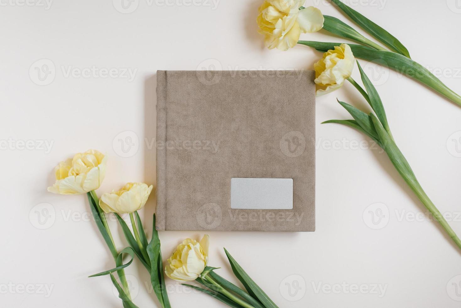 beige kleding stof familie of bruiloft foto album met leeg ruimte voor tekst omringd door geel tulpen Aan een licht achtergrond. familie foto archief