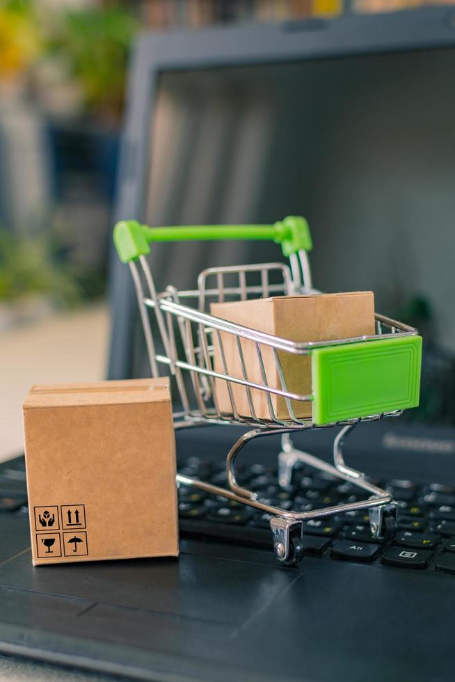 close-up van een winkelwagentje met een doos, naast een laptop en een creditcard, op het bureau. foto
