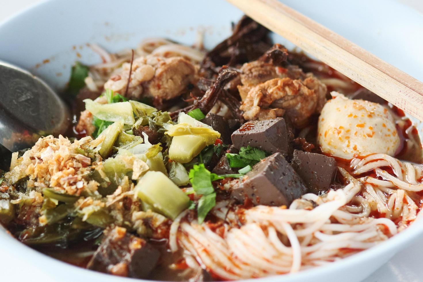 rijst- noedels met pittig varkensvlees saus in wit kom met eetstokjes en lepel. Thais pittig voedsel. foto