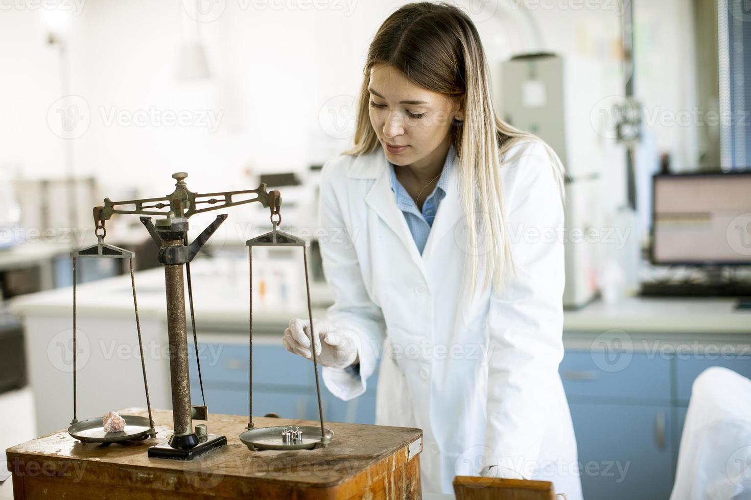jonge vrouwelijke onderzoeker die het gewicht van het mineraalmonster in het laboratorium meet foto