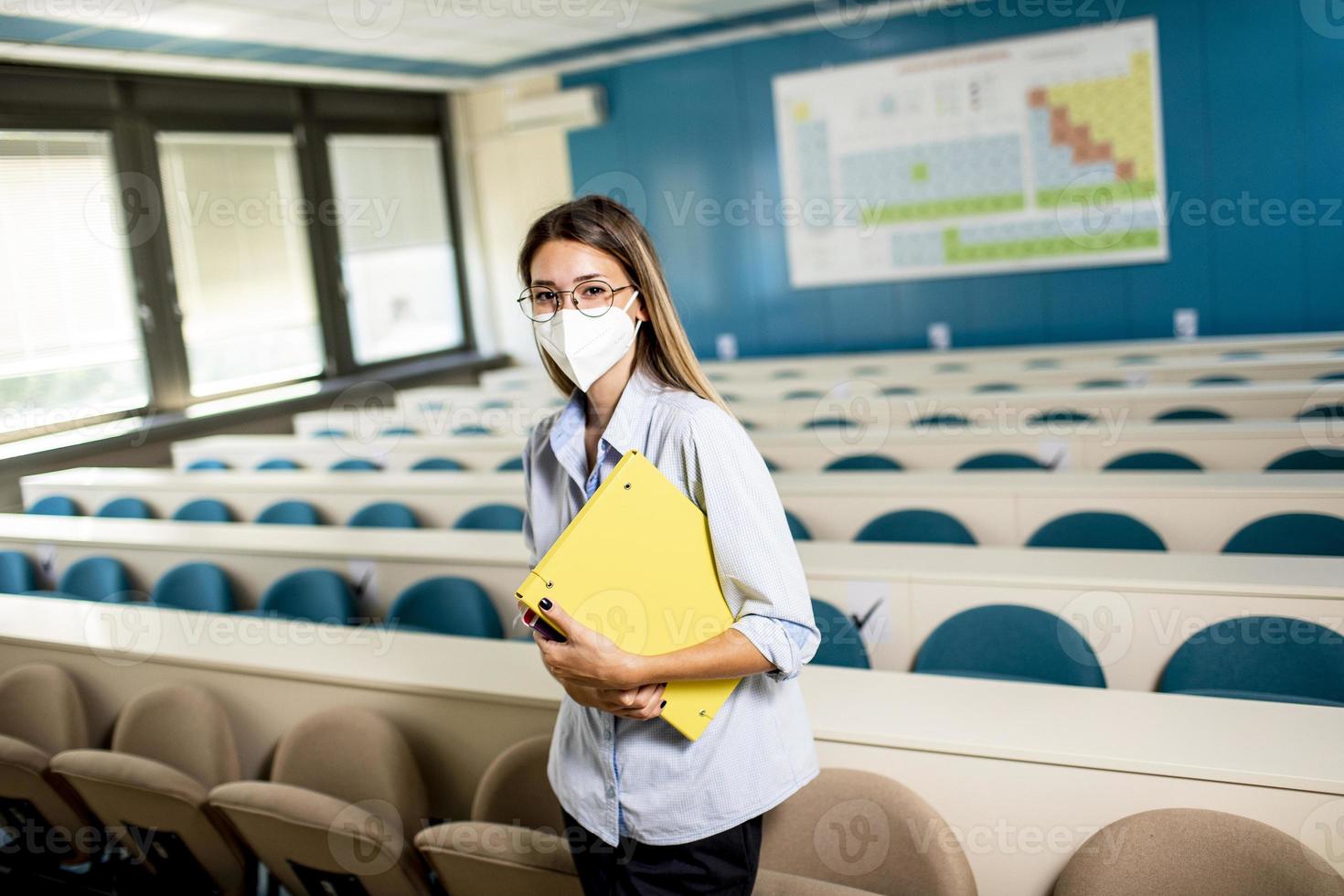 vrouwelijke student draagt gezicht beschermend medisch masker voor virusbescherming staande op collegezaal foto