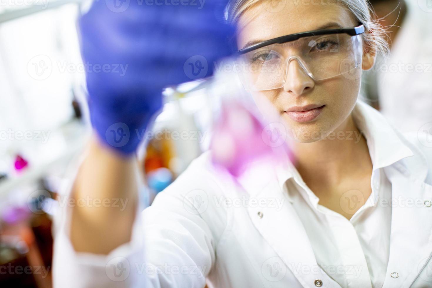 jonge vrouwelijke wetenschapper die vloeistof in biochemisch laboratorium onderzoekt foto