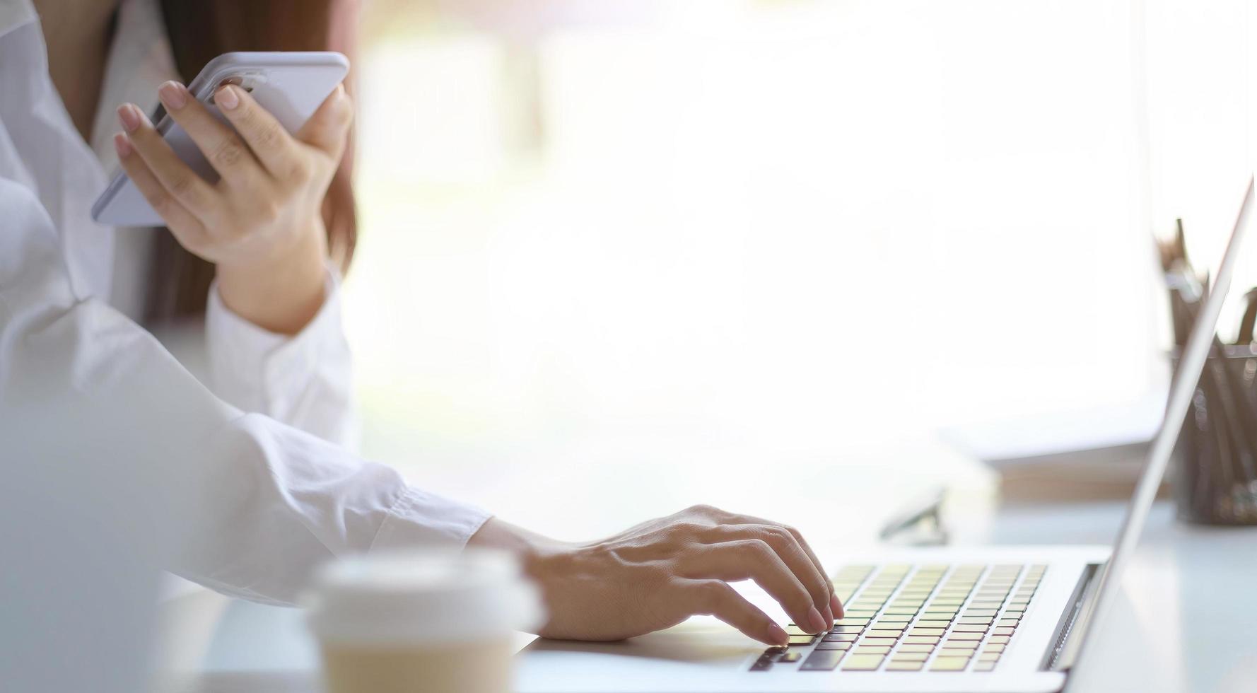 persoon die een telefoon gebruikt tijdens het typen op een laptop foto