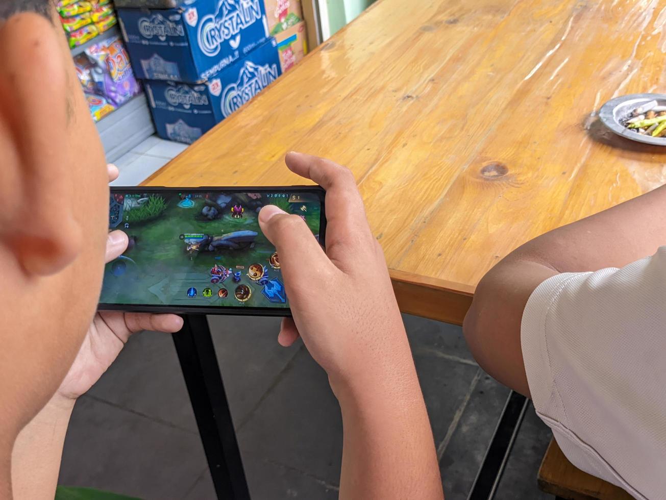 soera, Indonesië - april, 2023 - een Aziatisch jongen spelen mobiel legends spellen Aan smartphone foto