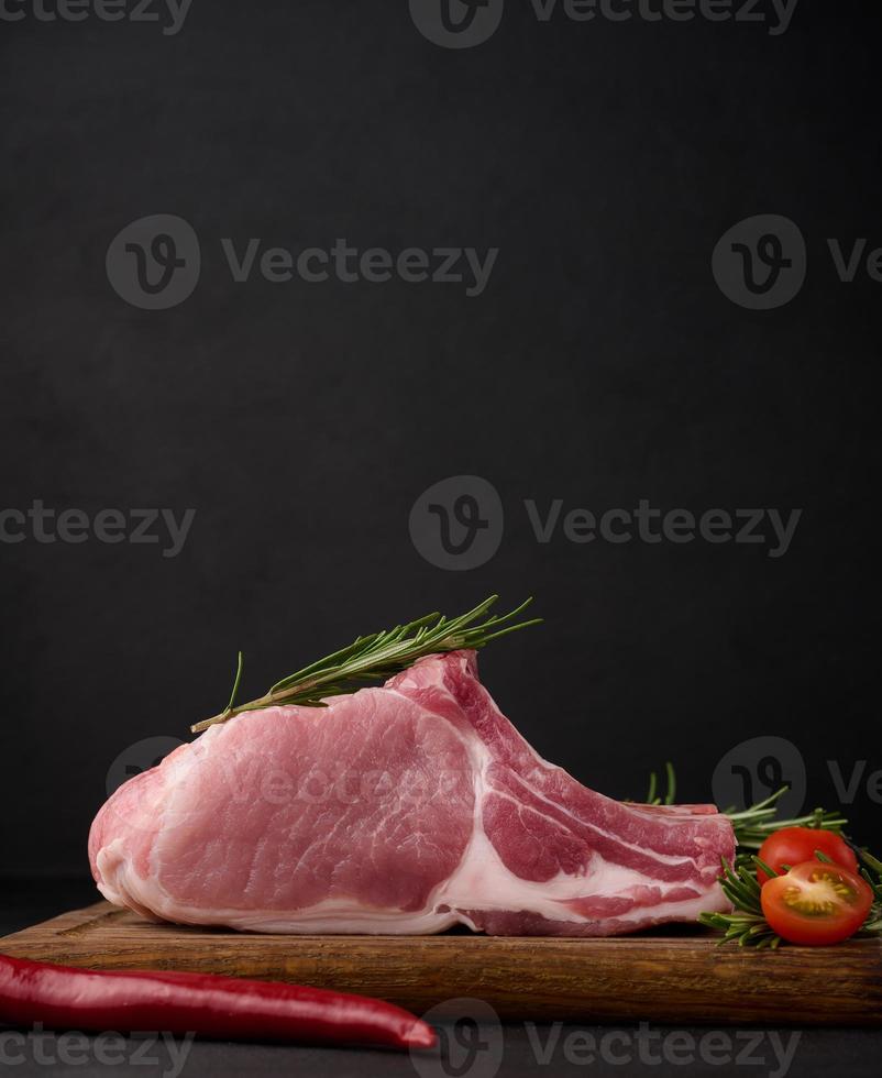 rauw varkensvlees lende Aan de bot en specerijen Aan een houten snijdend bord Aan een zwart achtergrond. deel voor lunch en avondeten foto