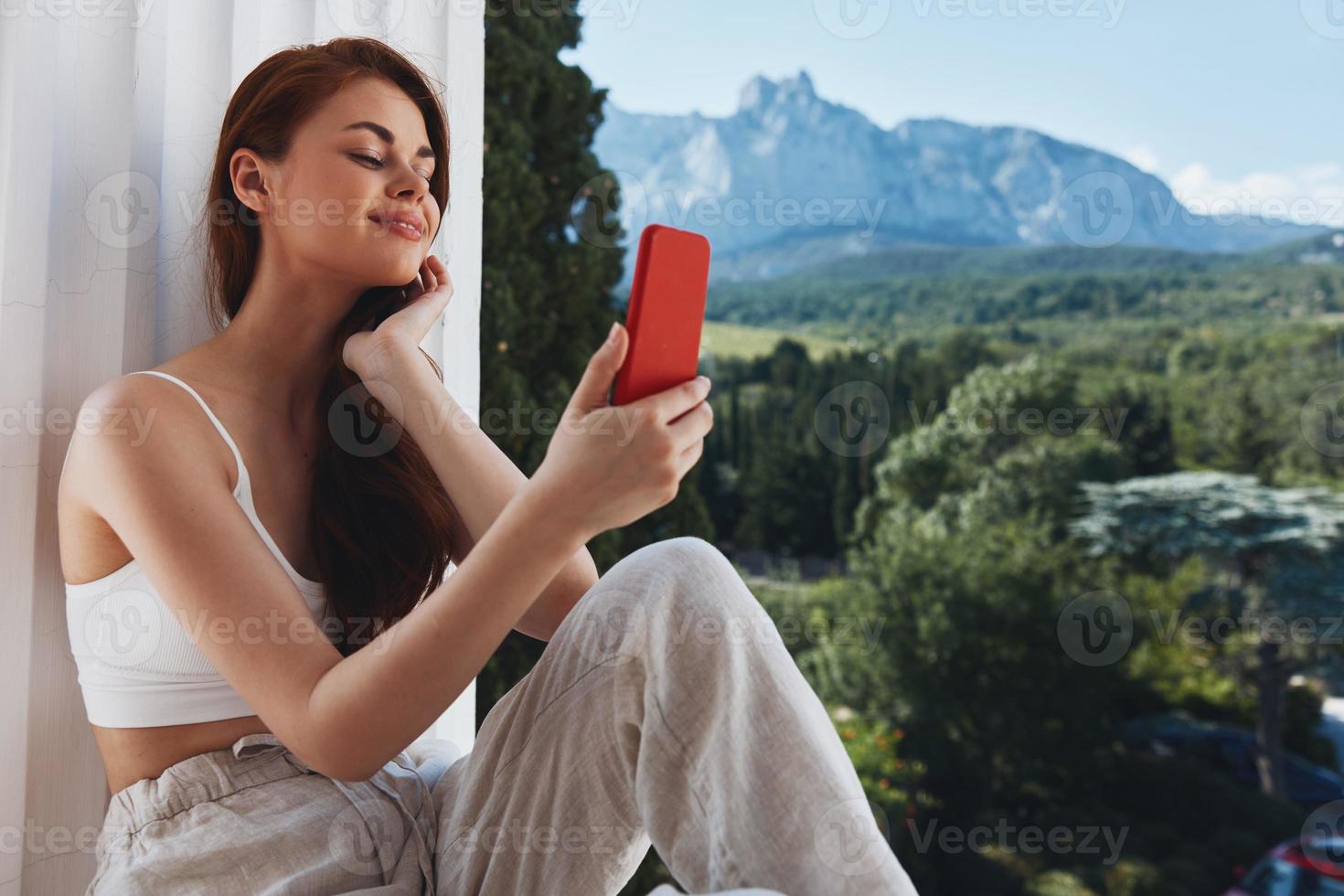 aantrekkelijk jong vrouw gebruik de telefoon looks Bij de scherm in een comfortabel hotel een Open visie van de berg visie foto