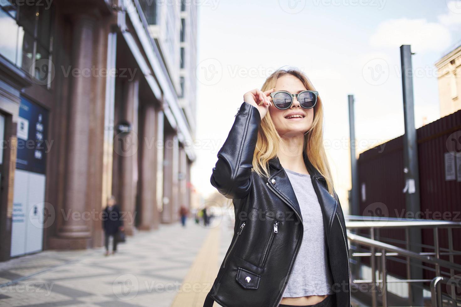 modieus vrouw in een leer jasje en zonnebril in de buurt de gebouw foto