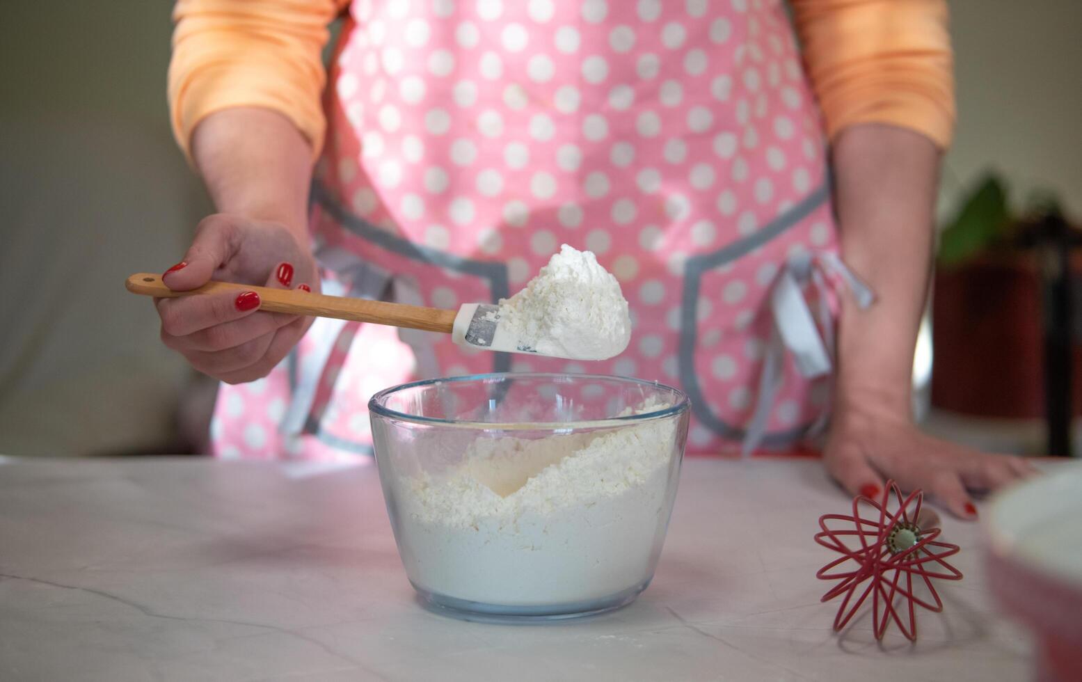 vrouw thuis bloem mengen in een glazen kom met een roze schort foto