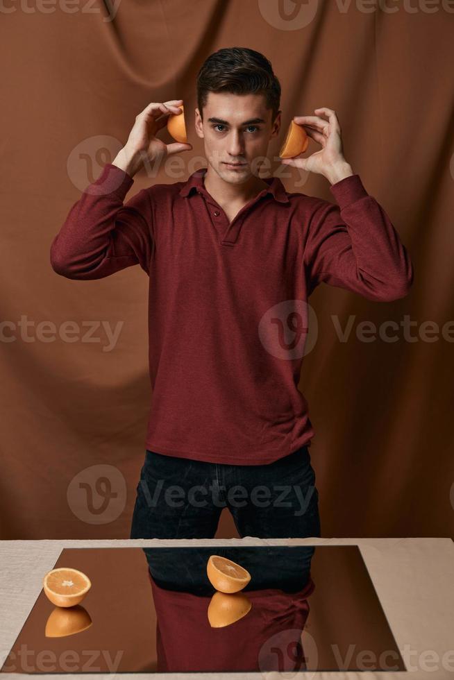 een knap Mens vervelend een rood overhemd met sinaasappels Holding een spiegel Aan de tafel foto