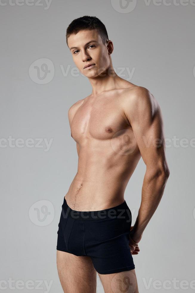 sportief Mens in zwart shorts Aan naakt lichaam grijs achtergrond spier bodybuilding geschiktheid foto