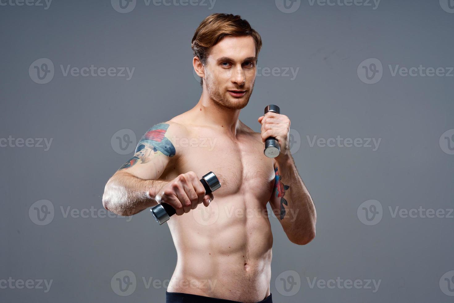 naakt atleet met een tatoeëren en halters in handen telefoon geschiktheid bodybuilding foto
