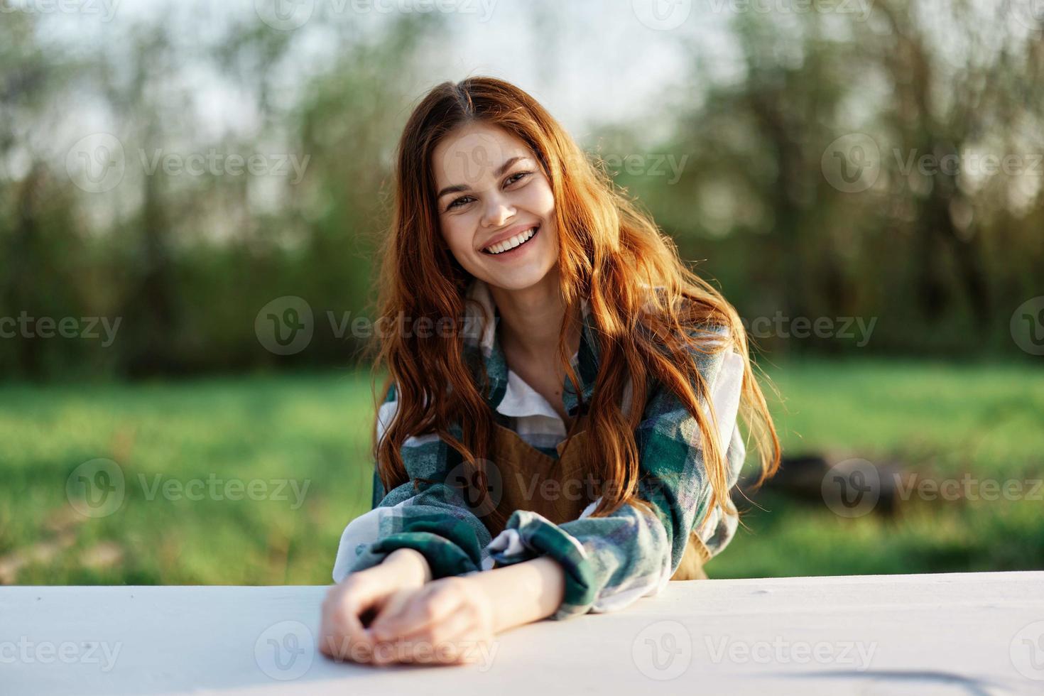 een mooi vrouw lacht met een toothy glimlach en geniet loungen in een groen park Aan een zomer avond in de instelling zonlicht. de concept van een gezond levensstijl en de bati van zelfzorg foto