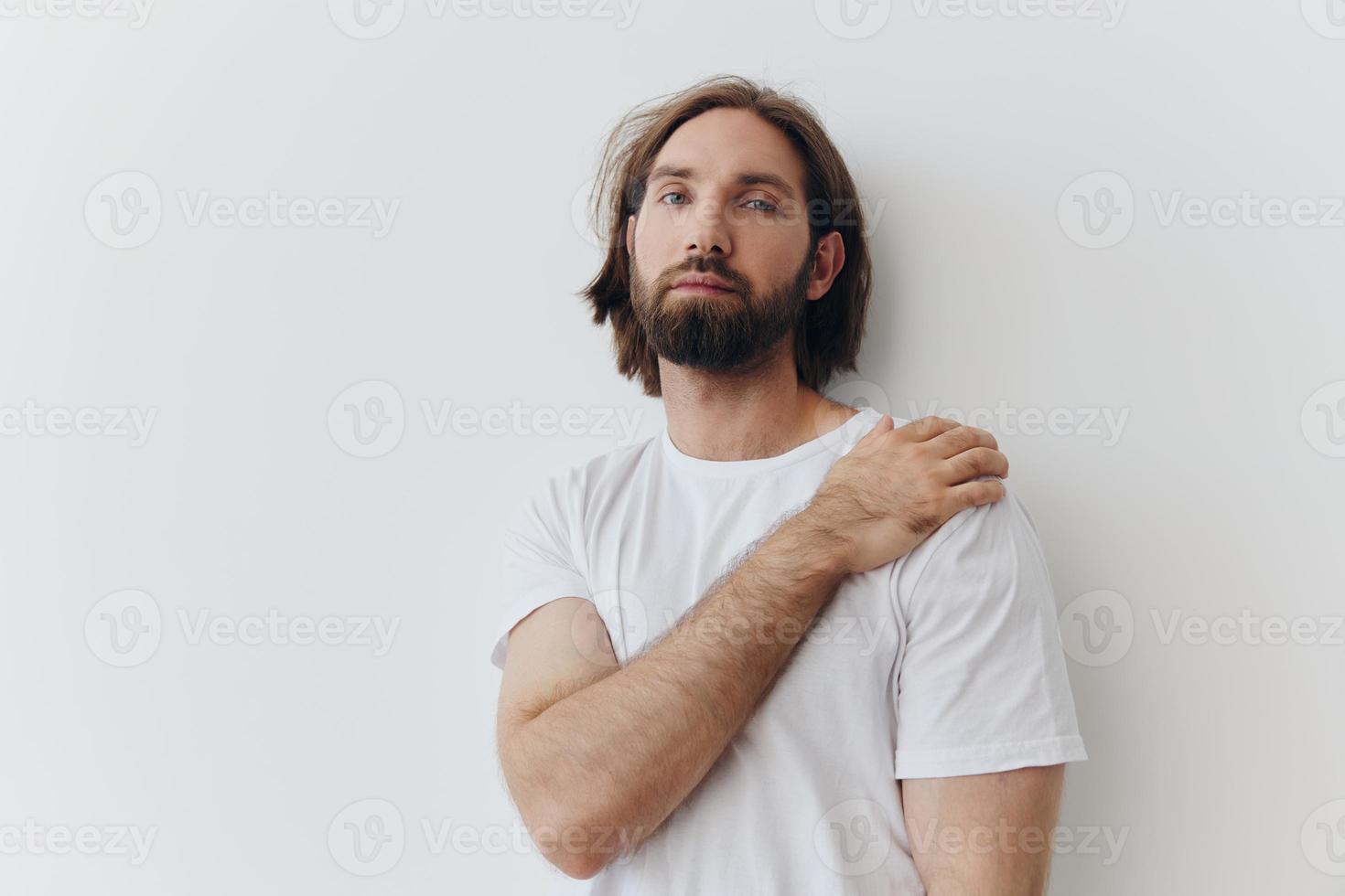 een Mens in een wit t-shirt en blauw jeans staat tegen een wit muur en poses foto