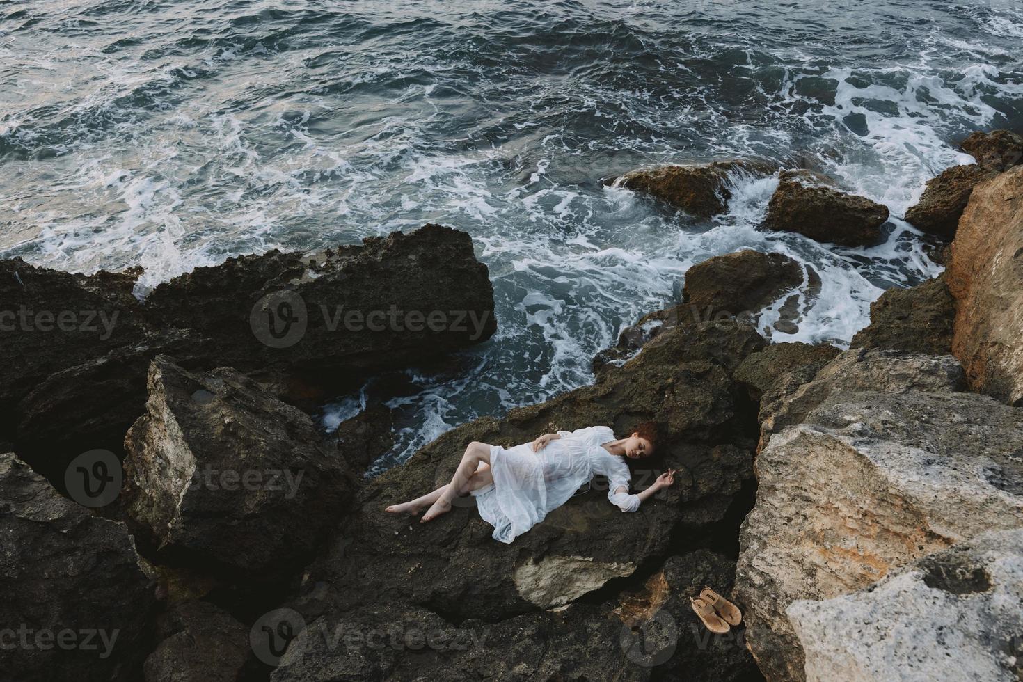 vrouw in een afgelegen plek Aan een wild rotsachtig kust in een wit jurk visie van bovenstaand foto