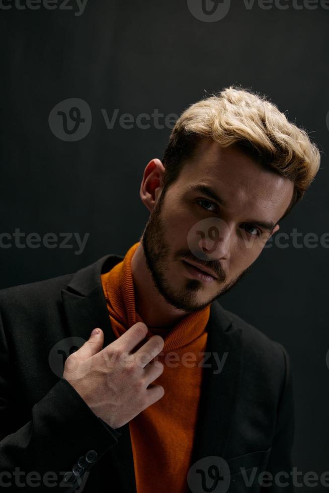 portret van een knap Mens in een jasje en een oranje trui gebaren met zijn handen donker achtergrond kopiëren ruimte foto