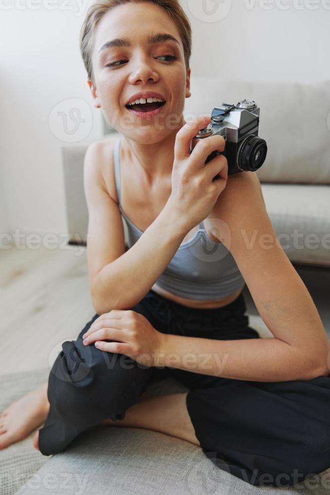 gelukkig glimlach vrouw Holding een oud camera en nemen afbeeldingen van haarzelf net zo een weekend fotograaf in huis kleren met een kort kapsel haar- zonder filters Aan een wit achtergrond, vrij kopiëren ruimte foto