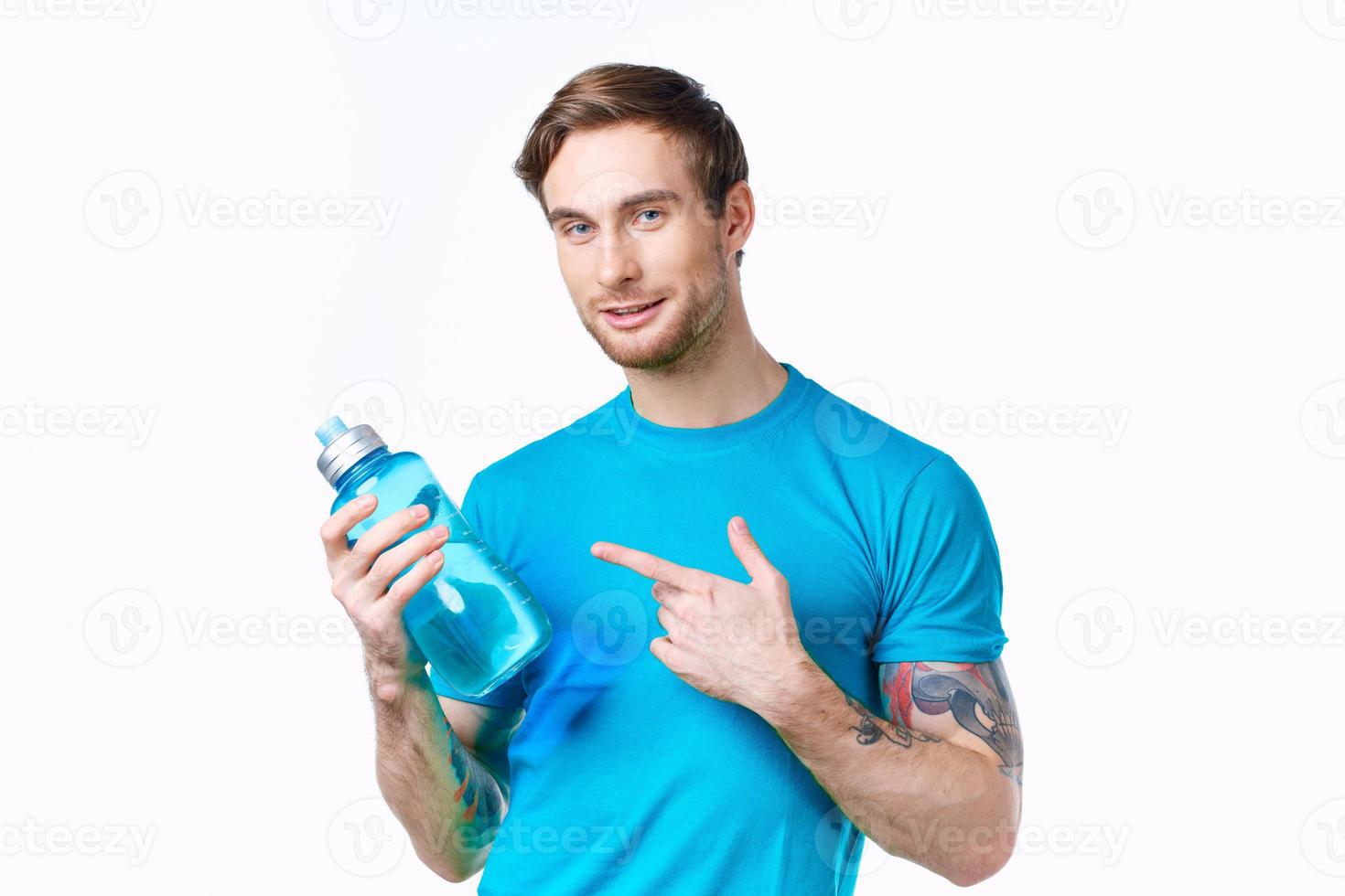 Mens in een blauw t-shirt met een fles van water in zijn hand- Aan een wit achtergrond kopiëren ruimte foto