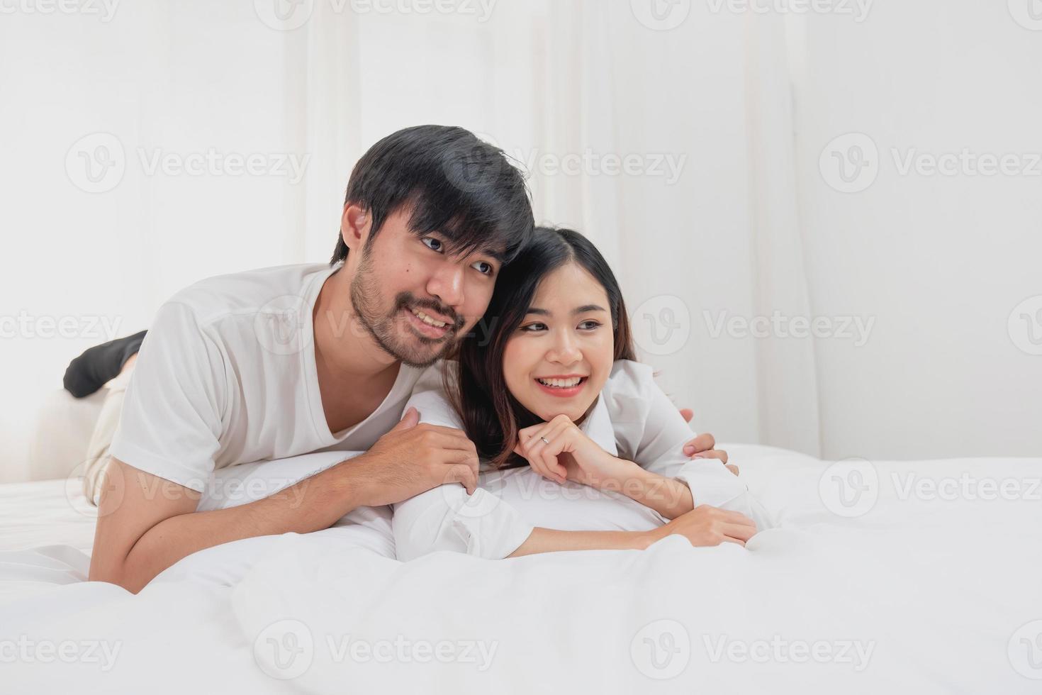 gelukkig jong Aziatisch paar omarmen, plagen, spelen vrolijk in bed Bij huis, romantisch tijd naar verbeteren familie binding. familie concept. foto