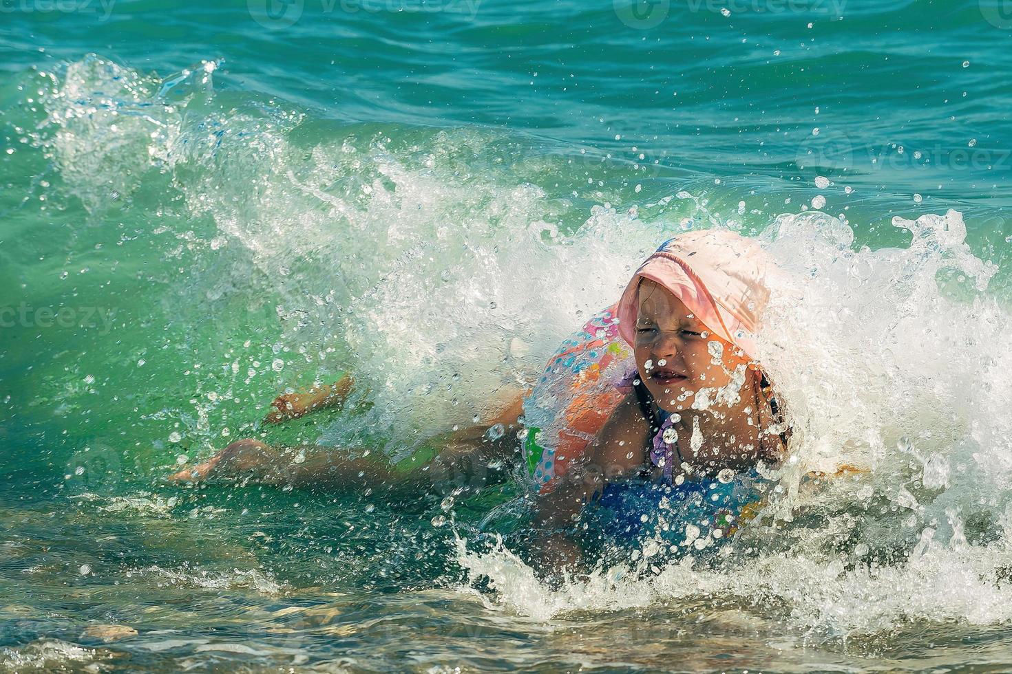 een weinig meisje in een zwempak en een zon hoed met een opblaasbaar ring heeft pret zwemmen Aan een zonnig dag in de zee foto