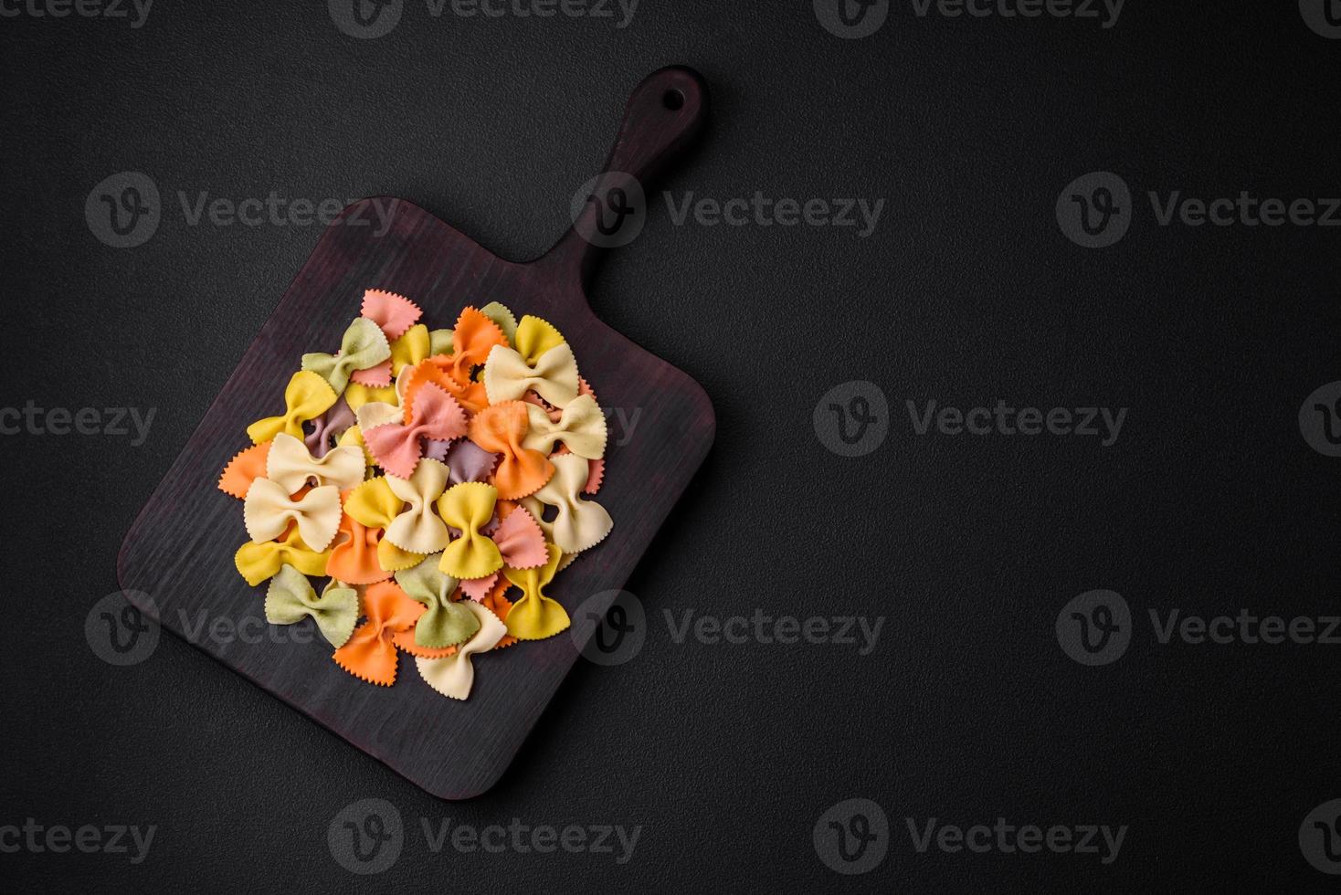 rauw farfalle pasta in verschillend kleuren Aan een donker beton achtergrond foto