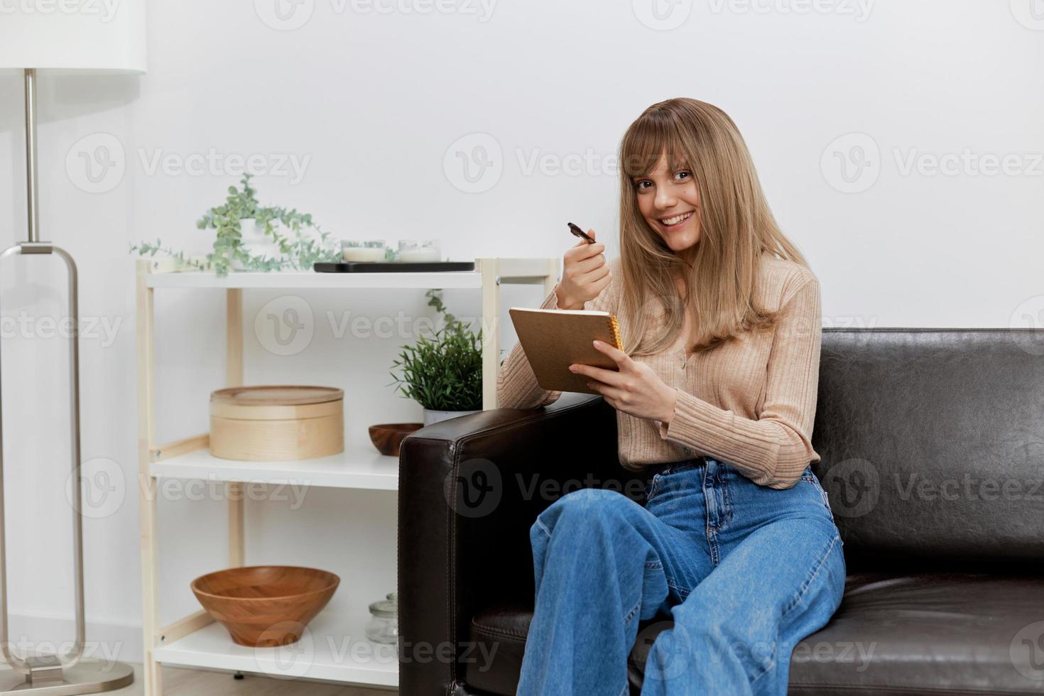 genoten blond leerling dame met schrijfboek points pen glimlacht Bij camera zittend in sofa Bij modern leven kamer. vrouw cliënt hebben krimpen afspraak in een psychologisch helpen kantoor. kopiëren ruimte foto