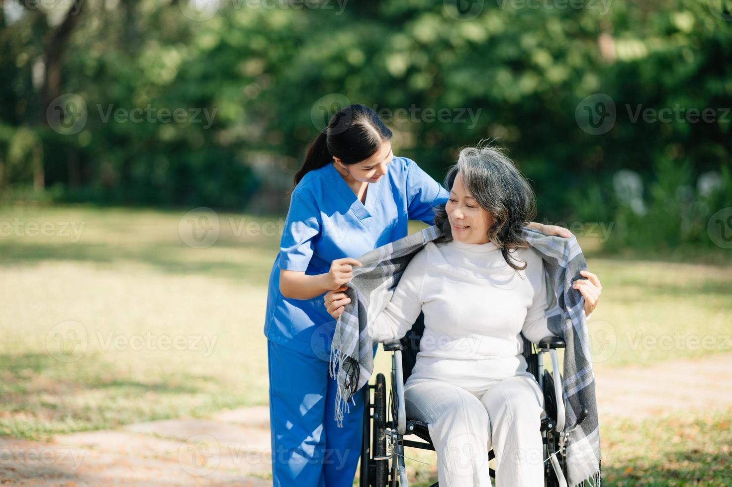 Aziatisch voorzichtig verzorger of verpleegster en de gelukkig geduldig in een rolstoel zijn wandelen in de tuin. naar helpen en aanmoedigen en rust uit uw geest met groen natuur. gebruik een stethoscoop naar luister naar uw foto