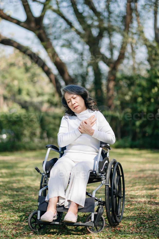 Aziatisch oud vrouw zittend Aan een rolstoel buitenshuis in de park hebben pijn in de armen, polsen en lichaam in zon licht foto