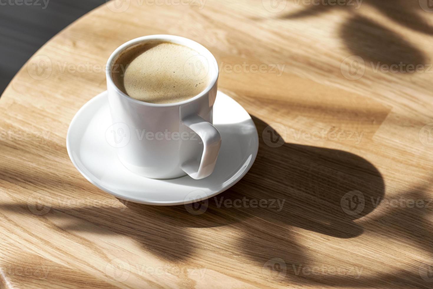 een wit porselein kop met koffie Aan een schotel staat Aan een ronde tafel foto