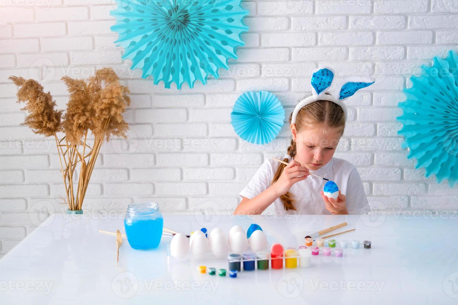weinig meisje schilderij eieren met blauw verf. gelukkig Pasen. kind maken Pasen decoratie Bij huis. foto