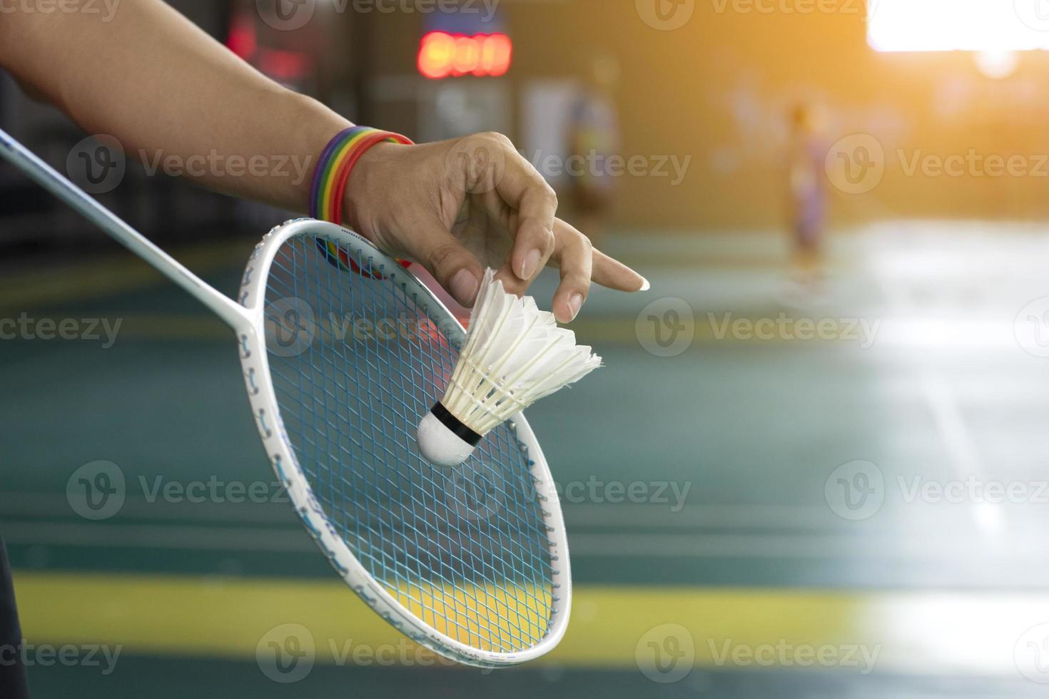 badminton speler draagt regenboog polsbandjes en Holding racket en wit shuttle in voorkant van de netto voordat portie het naar speler in een ander kant van de rechtbank, concept voor lgbt mensen activiteiten. foto