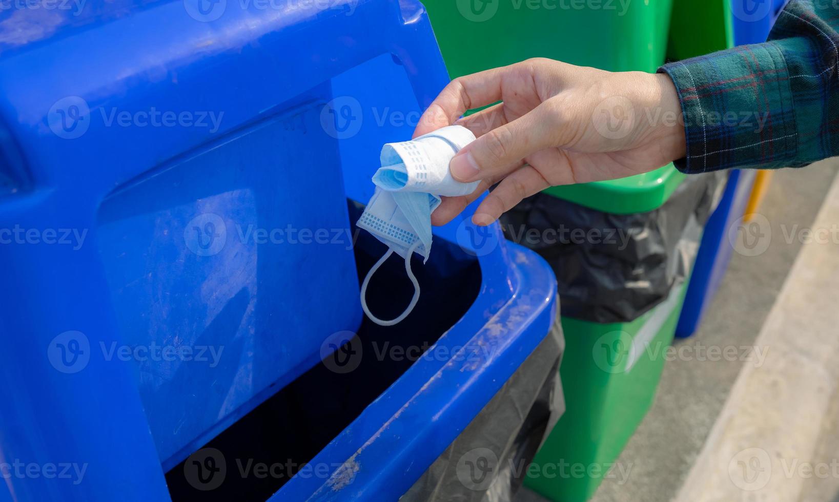 medisch afval. mensen hand- het werpen gebruikt medisch beschermend gezicht masker in recycle bak. blauw plastic recycle bak. Mens weggooien gebruikt masker in uitschot bak. gemeenschap medisch verspilling beheer. verspilling verschillend. foto