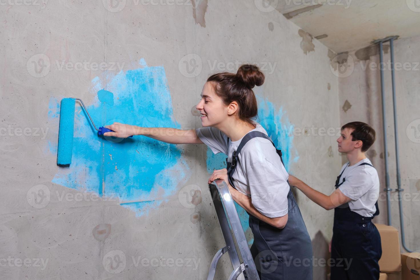 paar in nieuw huis gedurende reparatie werken schilderij muur samen. gelukkig familie Holding verf rol schilderij muur met blauw kleur verf in nieuw huis. huis vernieuwing diy vernieuwen huis concept. foto