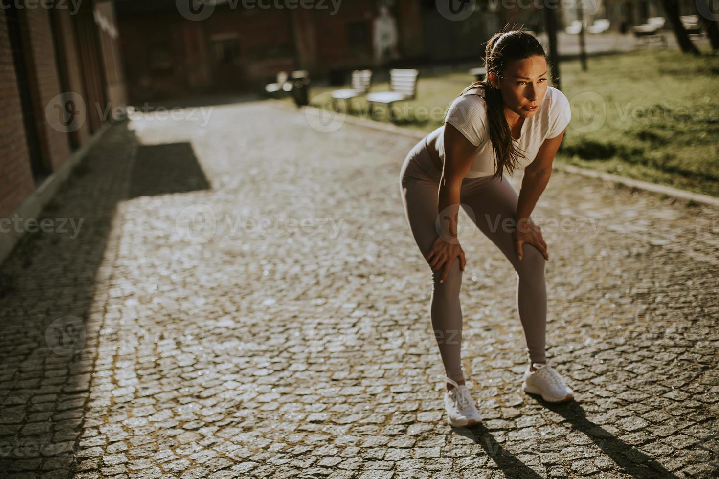 uitgeputte jonge vrouw die rust neemt tijdens training in de stedelijke omgeving foto