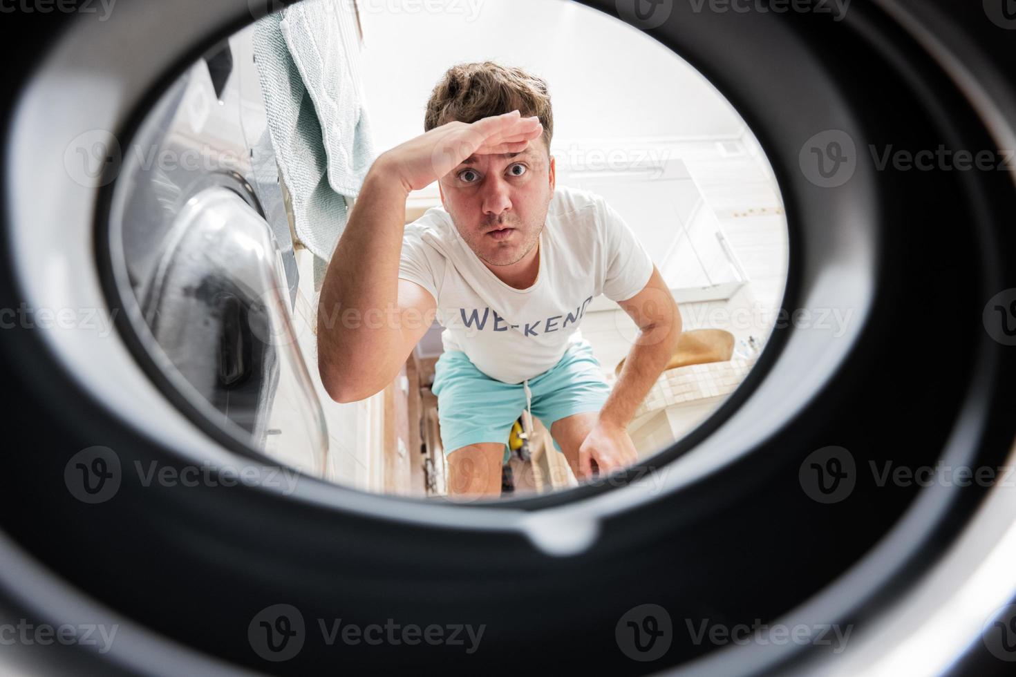 Mens visie van het wassen machine binnen. mannetje doet wasserij dagelijks routine. hand- over- voorhoofd op zoek ver weg, aan het kijken of zoeken. foto