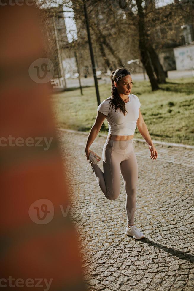 mooie jonge vrouw die zich uitstrekt tijdens de training in de stedelijke omgeving foto