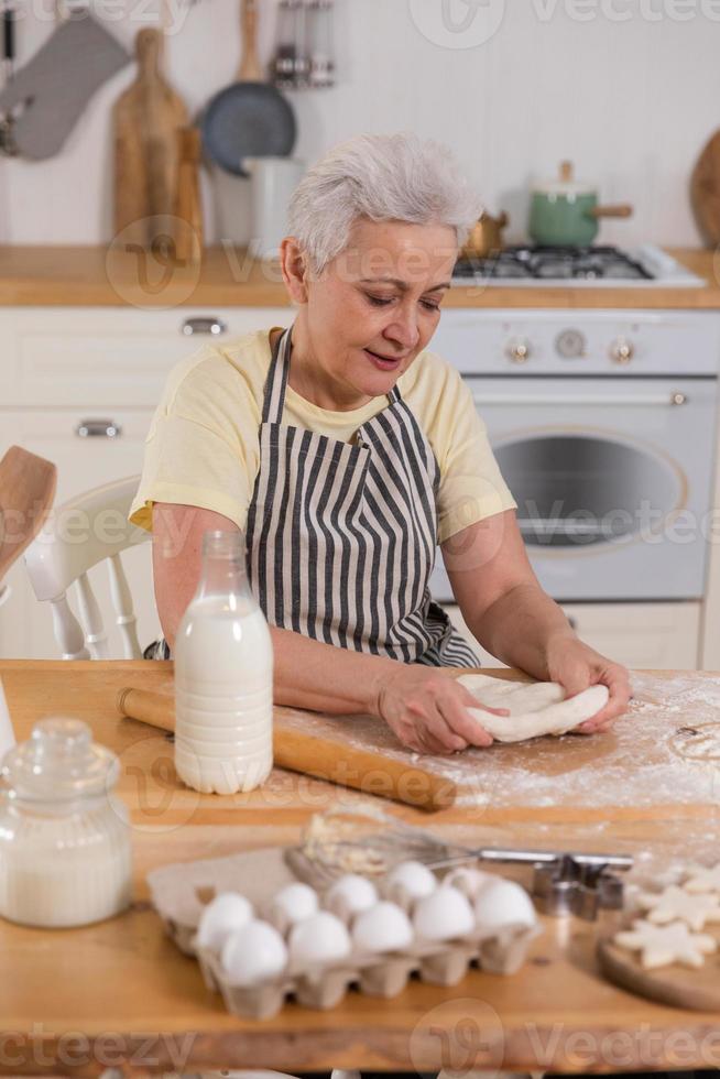 gelukkig senior vrouw Koken in keuken. elegant ouder volwassen grijs haren dame grootmoeder kneden deeg bakken koekjes. oud grootmoeder koken eigengemaakt voedsel. huishouden huisvrouw huiswerk concept. foto