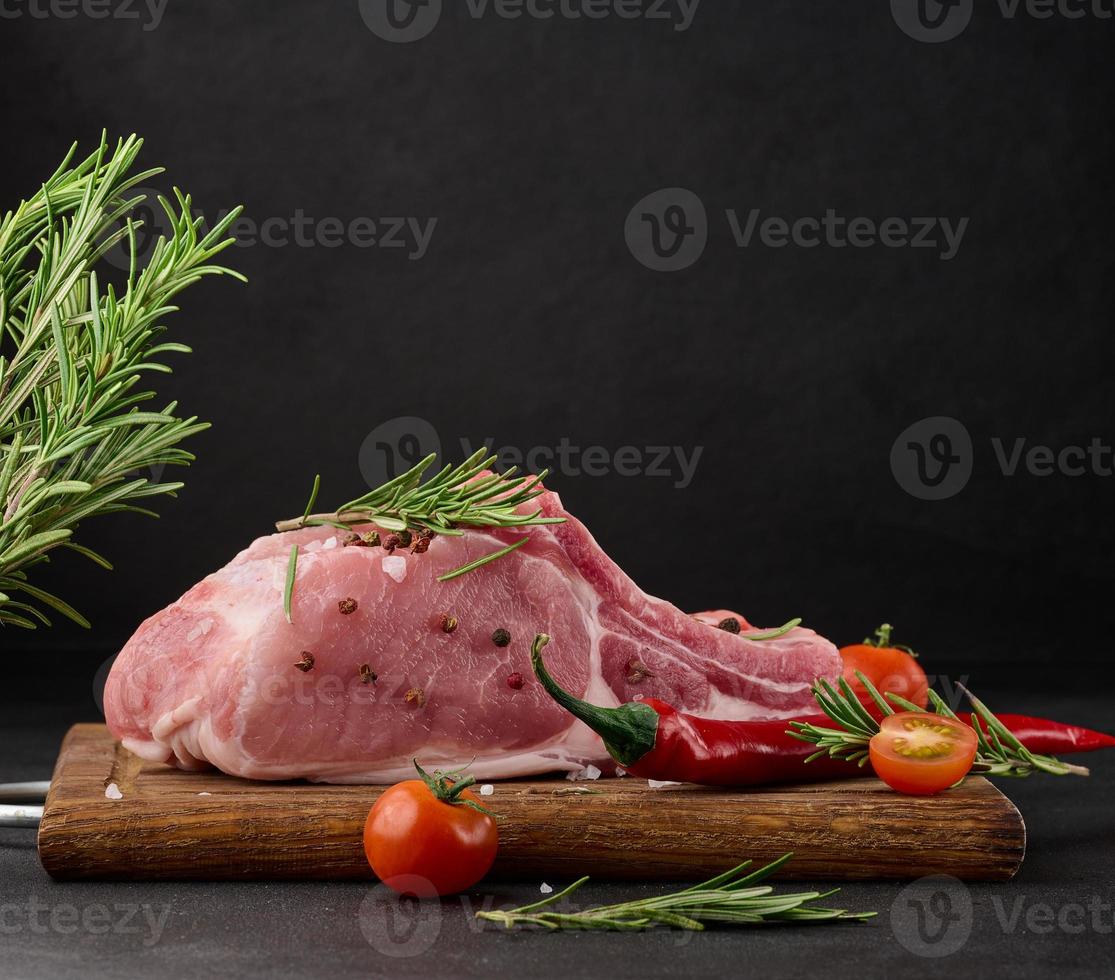 rauw varkensvlees lende Aan de bot en specerijen Aan een houten snijdend bord Aan een zwart achtergrond. deel voor lunch en avondeten foto