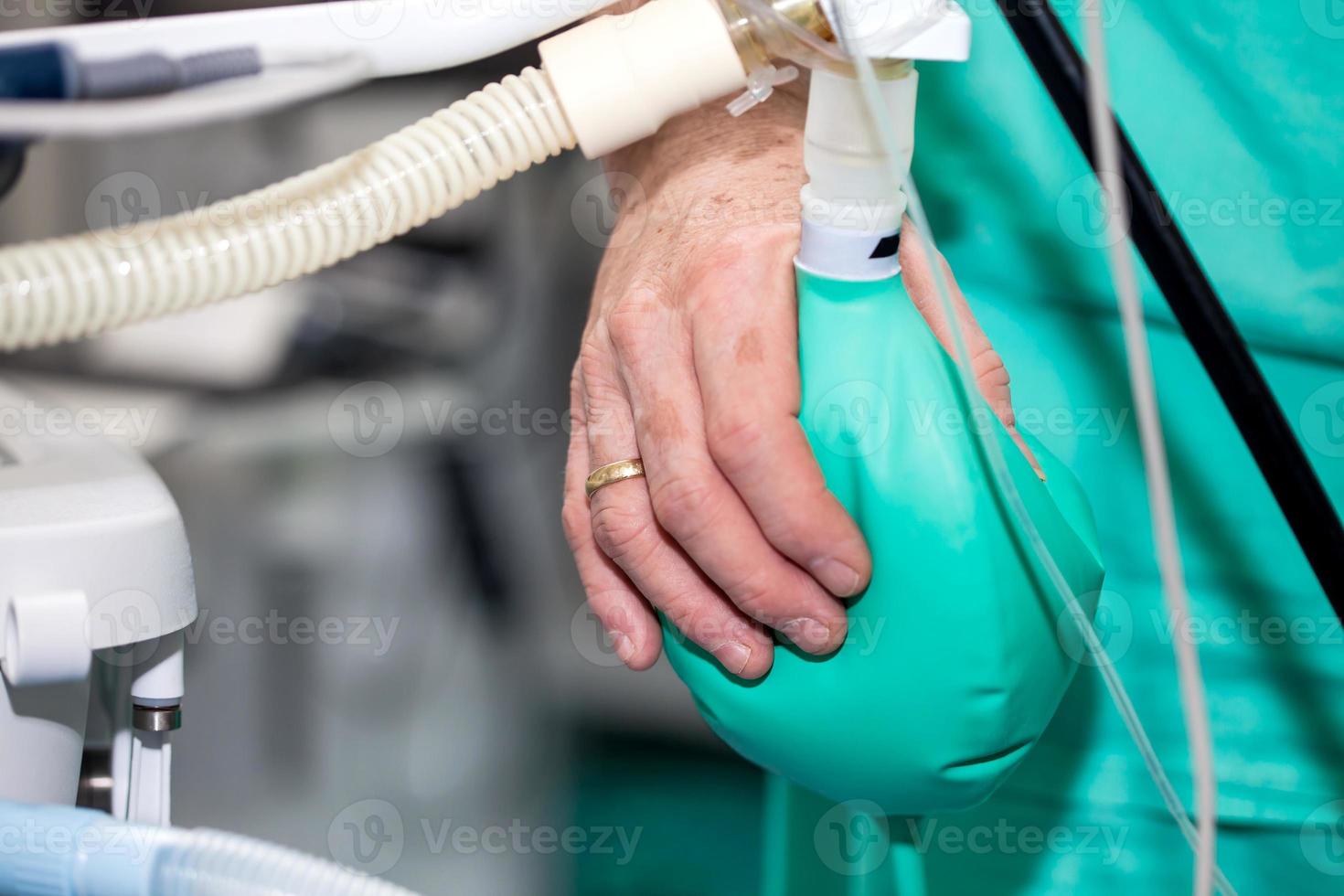 dichtbij omhoog van een dokter hand- drukken de anesthesie herademen zak terwijl chirurgisch team bereidt zich voor hun geduldig voor chirurgie foto