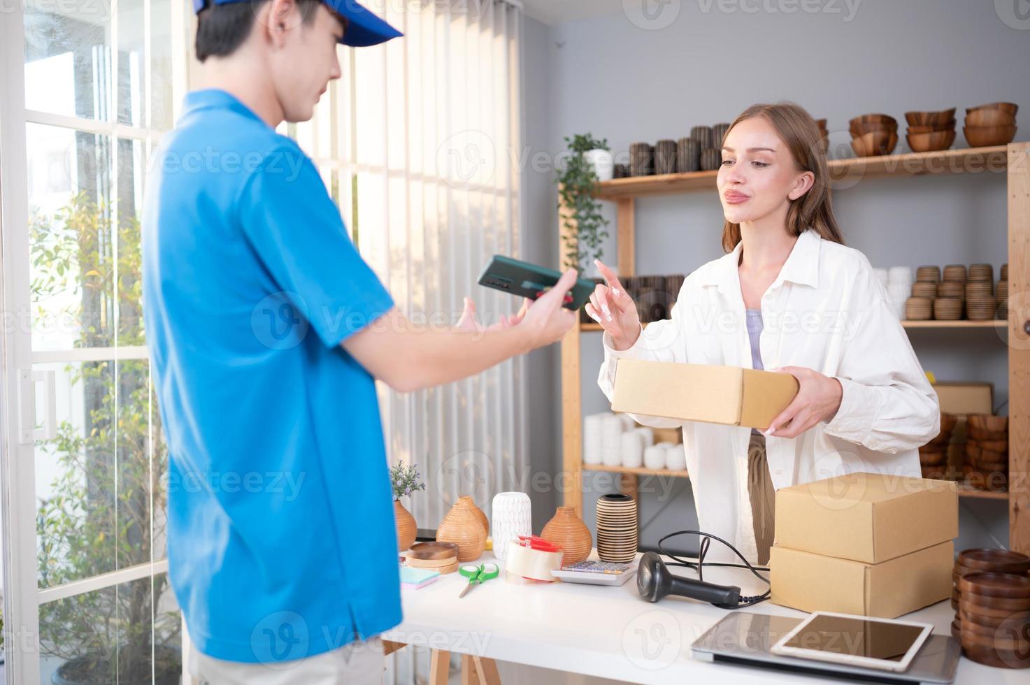 jong vrouw tekens haar naam Aan een smartphone na ontvangen een doos van items van de levering persoon. foto