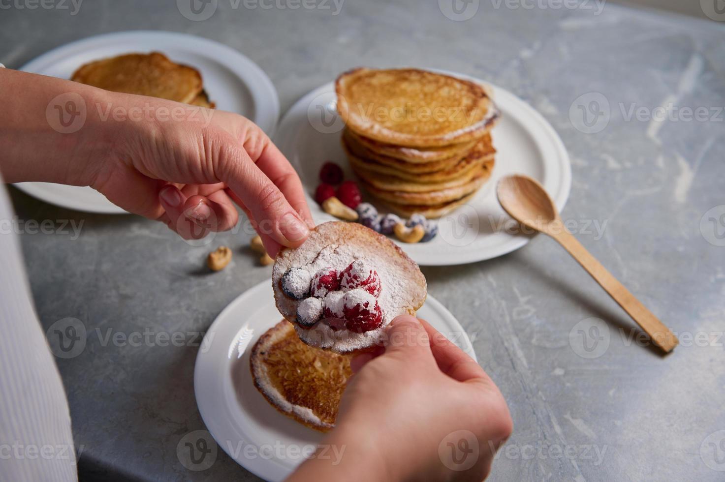 top visie van de handen van vrouw chef, huisvrouw met eigengemaakt pannekoeken besprenkeld met suikerglazuur suiker Aan een wit bord. voedsel achtergrond, Koken Aan vastenavond, vasten dinsdag concept foto