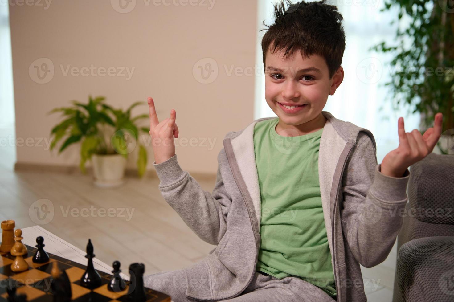gelukkig tiener- jongen glimlacht op zoek Bij camera, genieten van spelen schaak spel in de huis interieur foto