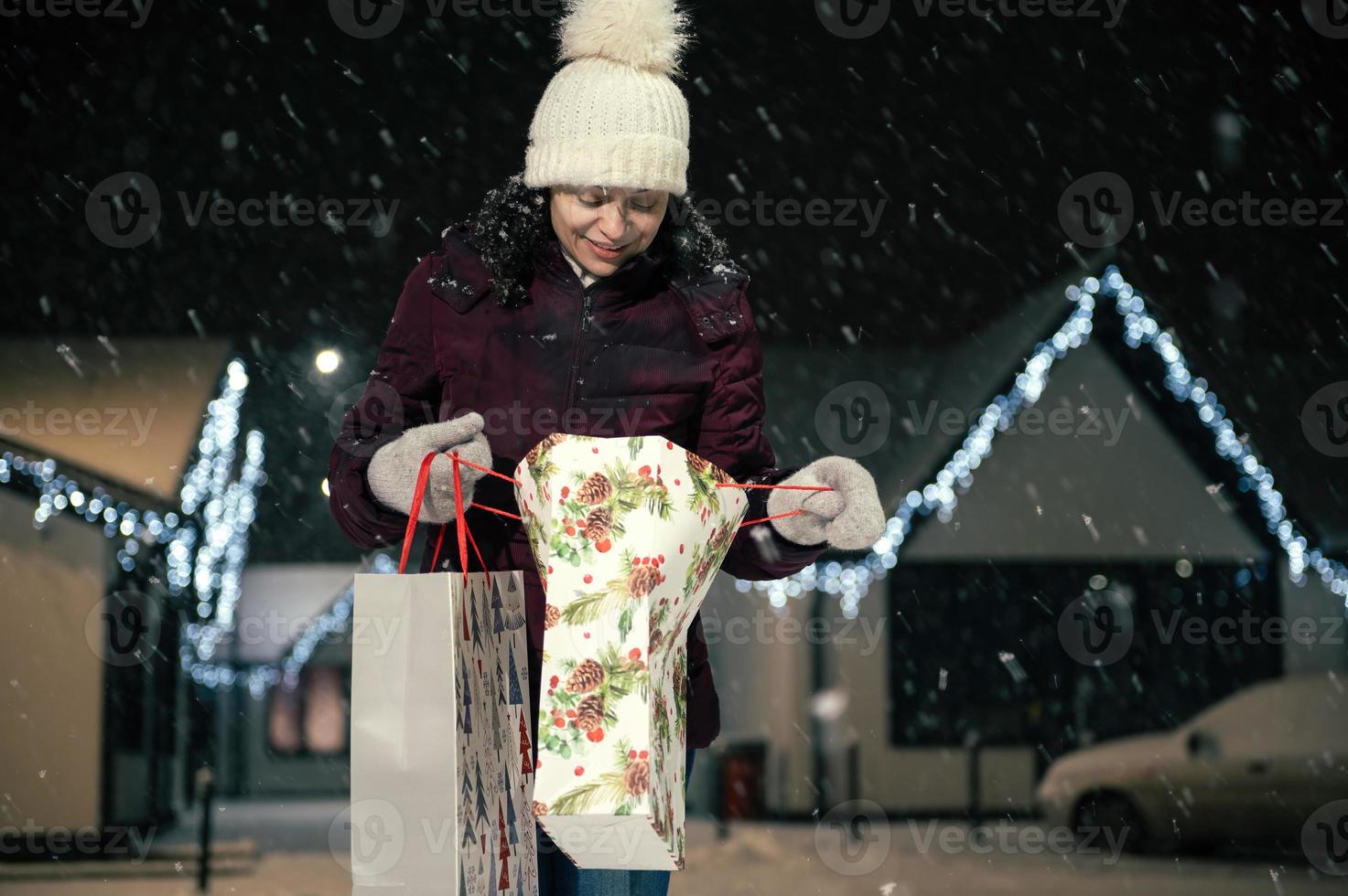 mooi vrouw met boodschappen doen Tassen wandelen naar beneden de sneeuw gedekt straat Aan een besneeuwd winter verkoudheid avond foto