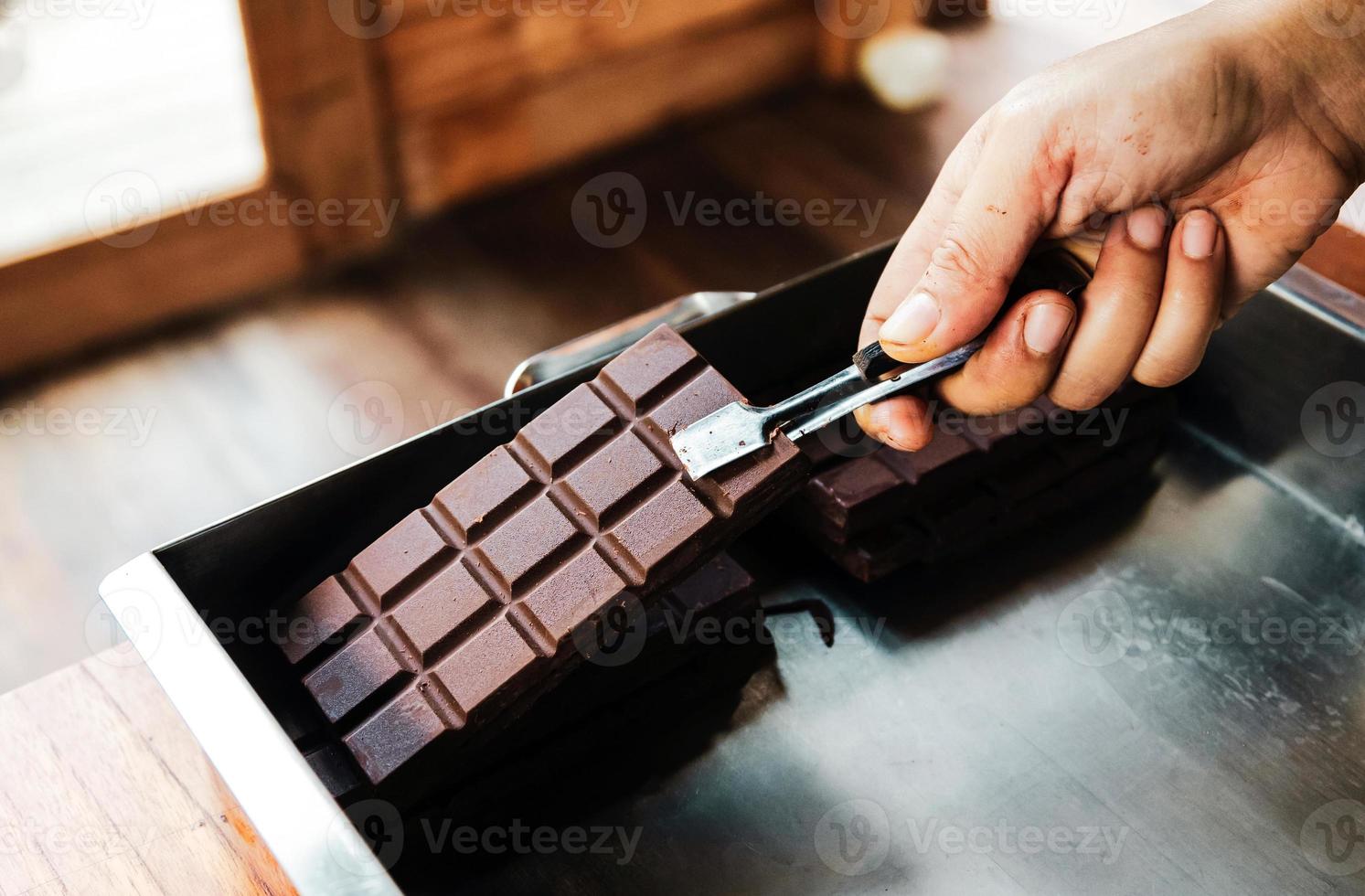 hand- van hulp in de huishouding gebruik makend van tang eigengemaakt vers donker chocola bar. een detailopname chocola bar en cacao achtergrond foto