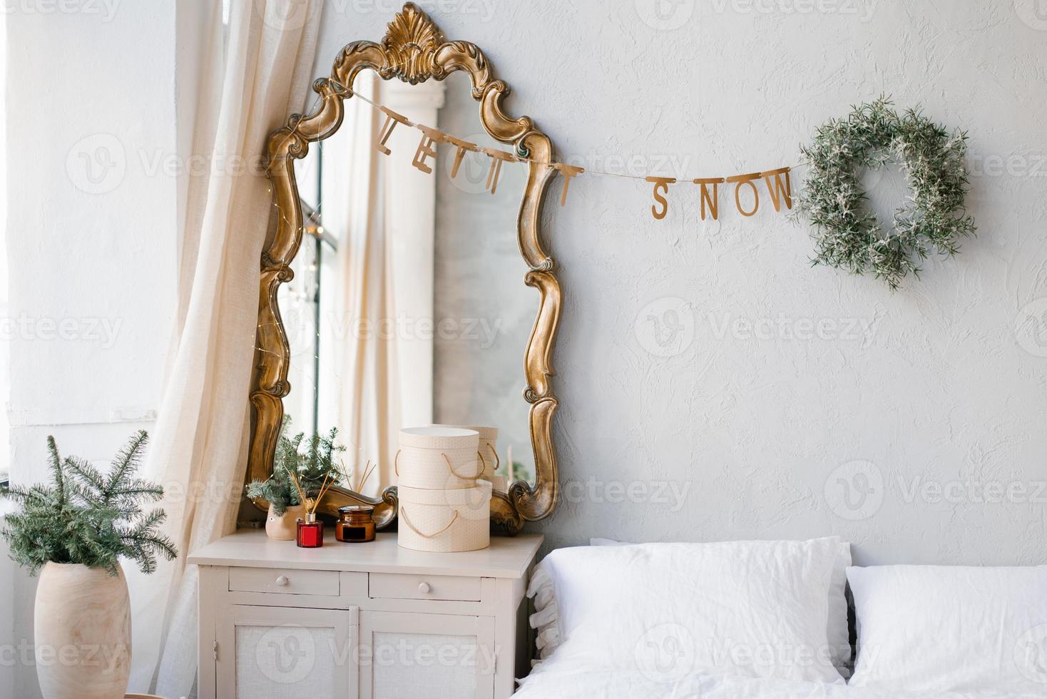 de interieur van een slaapkamer versierd voor Kerstmis en nieuw jaar in een Scandinavisch of wijnoogst stijl. een spiegel over- de dressoir, net takken in een vaas, een Kerstmis krans over- de bed foto
