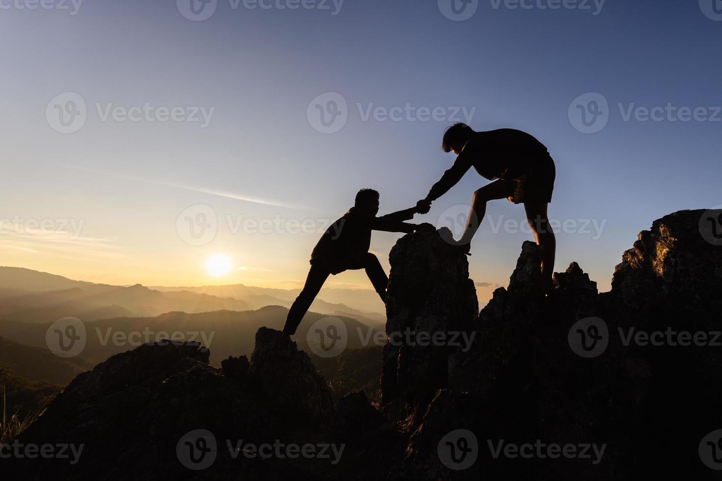 silhouet teamwerk, mannetje wandelaars beklimming omhoog berg klif en een van hen geven helpen hand. mensen helpen en, team werk concept. foto