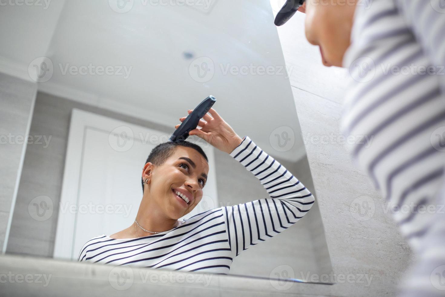 spiegel reflectie van kort haren vrouw in tank top gebruik makend van haar knippen machine foto